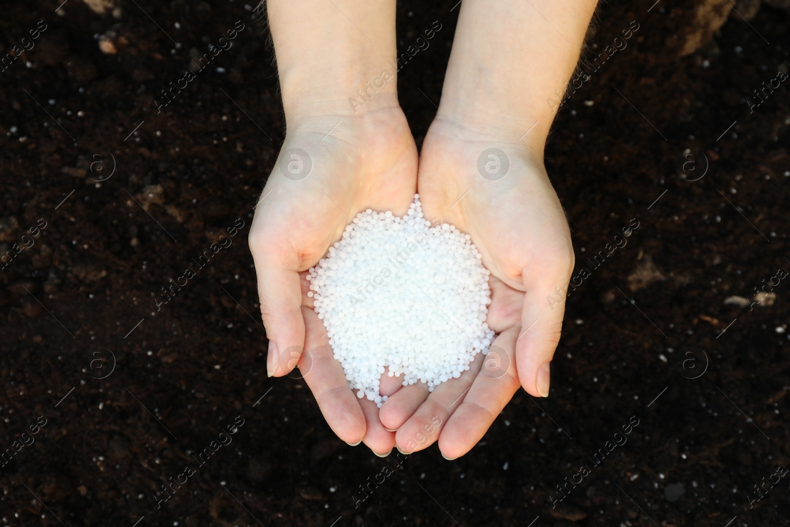 Photo of Woman holding plant fertilizer over soil outdoors, top view