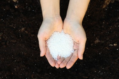 Photo of Woman holding plant fertilizer over soil outdoors, top view