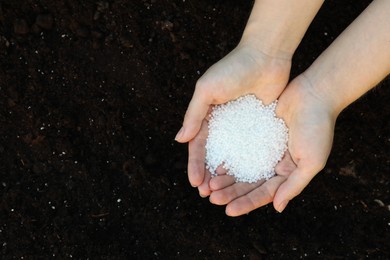 Photo of Woman holding plant fertilizer over soil outdoors, top view. Space for text