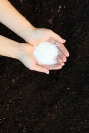 Photo of Woman holding plant fertilizer over soil outdoors, top view