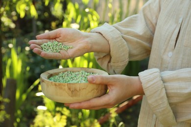 Woman holding plant fertilizer in bowl outdoors, closeup