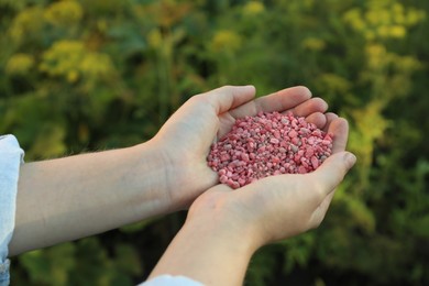 Photo of Woman holding pink plant fertilizer outdoors, closeup