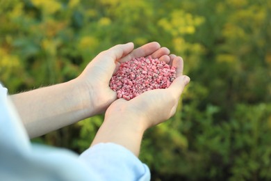 Photo of Woman holding pink plant fertilizer outdoors, closeup