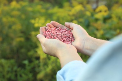 Photo of Woman holding pink plant fertilizer outdoors, closeup