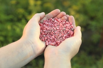 Photo of Woman holding pink plant fertilizer outdoors, closeup