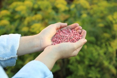 Woman holding pink plant fertilizer outdoors, closeup