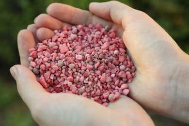 Photo of Woman holding pink plant fertilizer outdoors, closeup