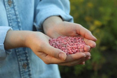 Photo of Woman holding pink plant fertilizer outdoors, closeup