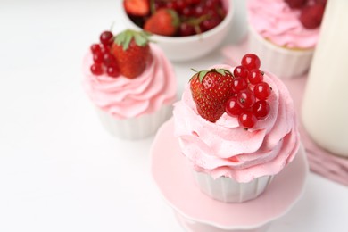 Photo of Tasty cupcakes with strawberries and red currants on white table, closeup. Space for text