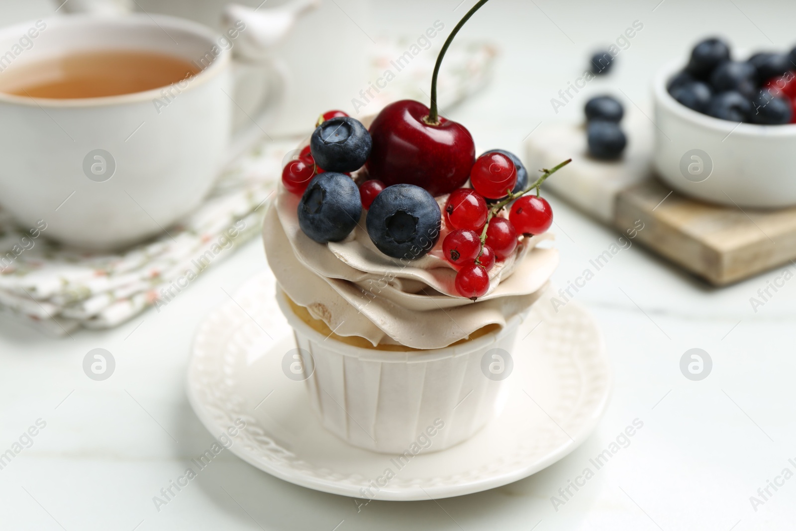 Photo of Tasty cupcake with different berries and tea on white marble table, closeup