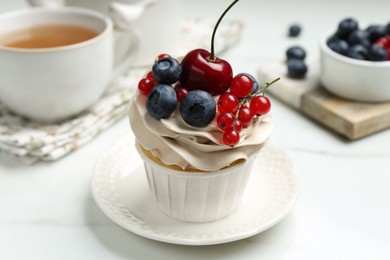 Tasty cupcake with different berries and tea on white marble table, closeup