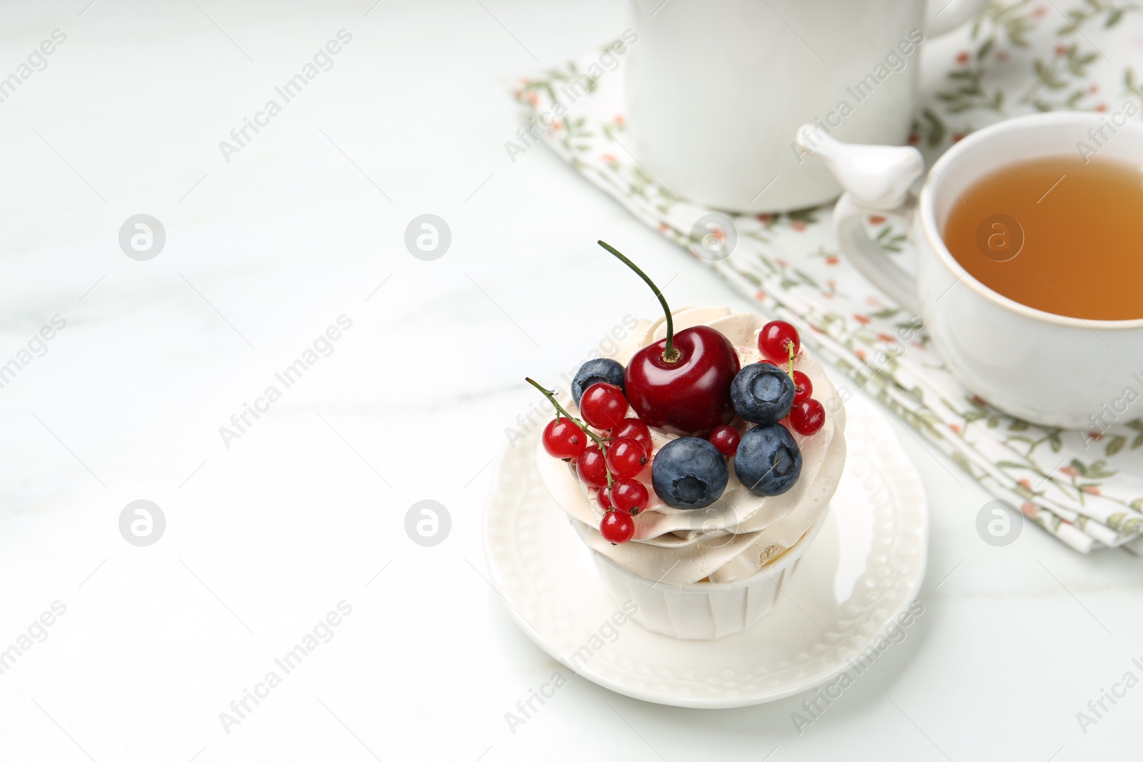 Photo of Tasty cupcake with different berries and tea on white marble table, space for text