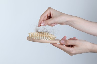 Woman taking lost hair from brush on light grey background, closeup. Space for text