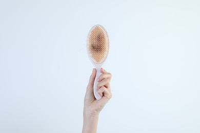 Woman holding brush with lost hair on light grey background, closeup