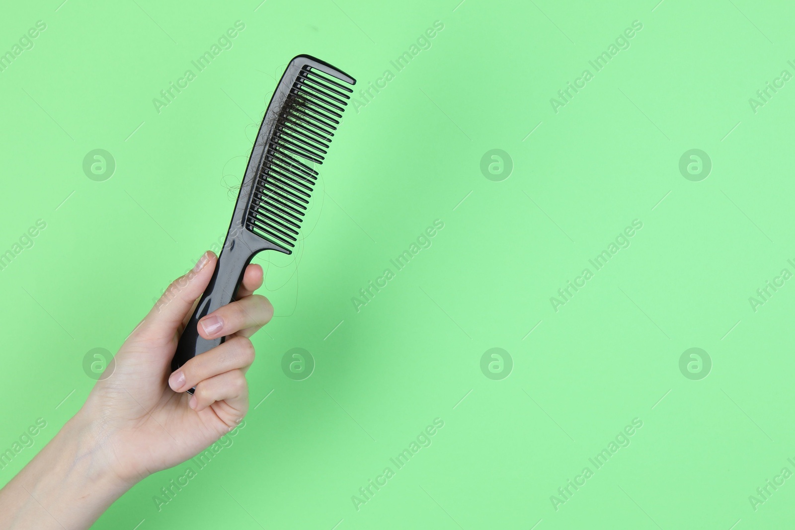 Photo of Woman holding comb with lost hair on green background, closeup. Space for text