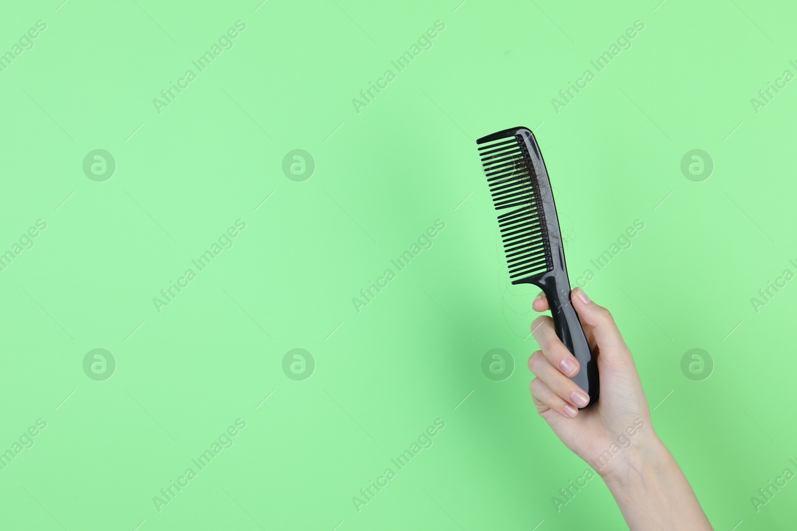 Photo of Woman holding comb with lost hair on green background, closeup. Space for text