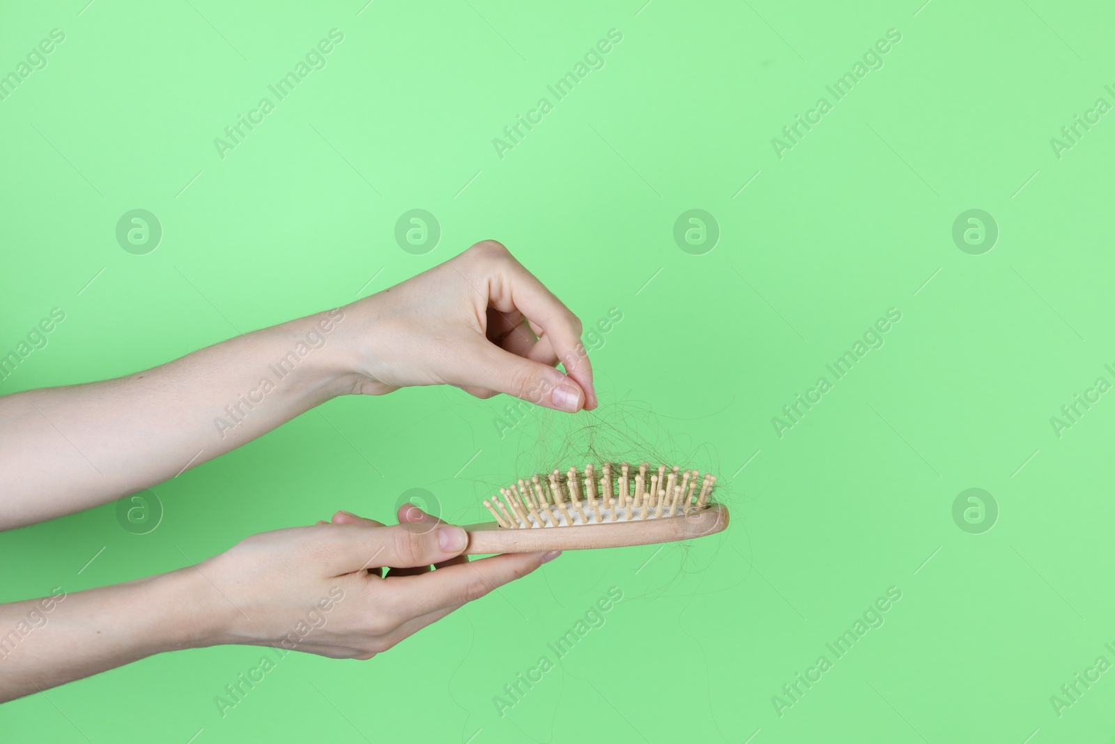 Photo of Woman taking lost hair from brush on green background, closeup. Space for text