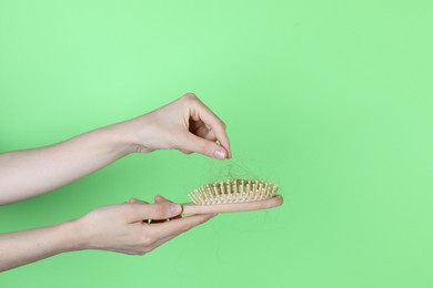 Woman taking lost hair from brush on green background, closeup. Space for text