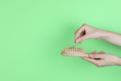 Woman taking lost hair from brush on green background, closeup. Space for text