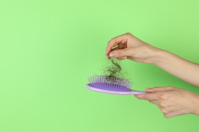 Woman taking lost hair from brush on green background, closeup. Space for text