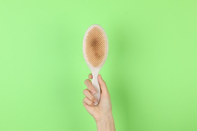 Photo of Woman holding brush with lost hair on green background, closeup