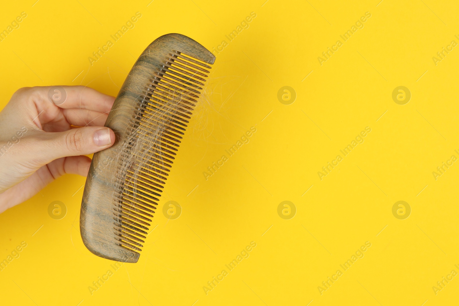 Photo of Woman holding comb with lost hair on yellow background, closeup. Space for text