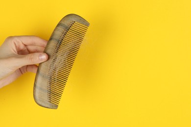 Woman holding comb with lost hair on yellow background, closeup. Space for text