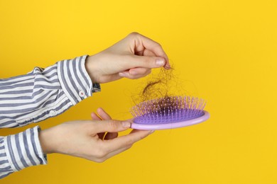 Woman taking lost hair from brush on yellow background, closeup