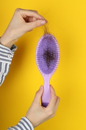 Photo of Woman taking lost hair from brush on yellow background, closeup