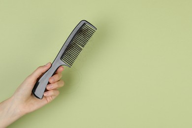 Photo of Woman holding comb with lost hair on olive background, closeup. Space for text