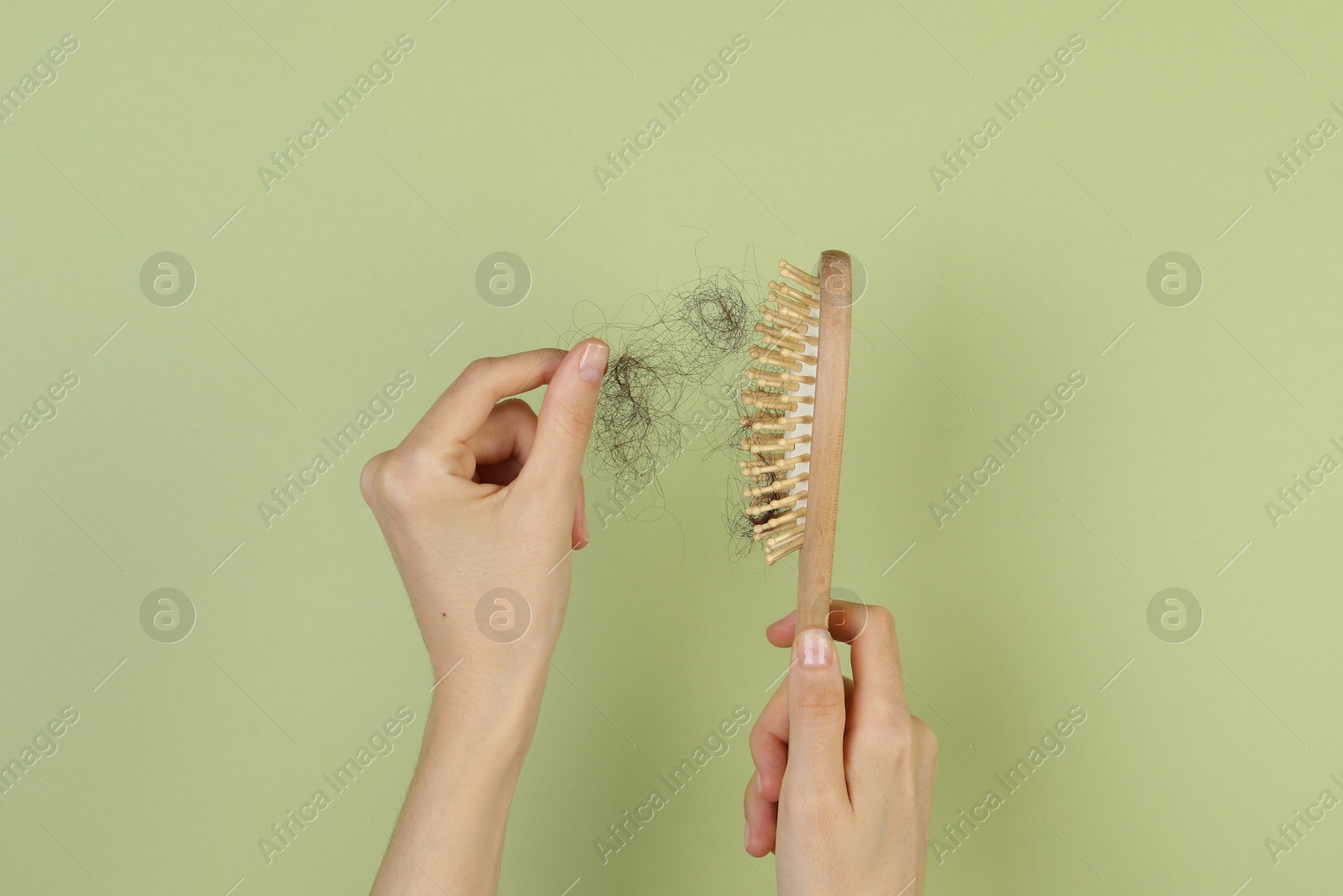 Photo of Woman taking lost hair from brush on olive background, top view