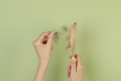 Woman taking lost hair from brush on olive background, top view