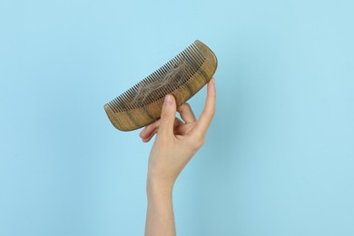 Woman holding comb with lost hair on light blue background, closeup