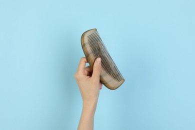 Photo of Woman holding comb with lost hair on light blue background, closeup