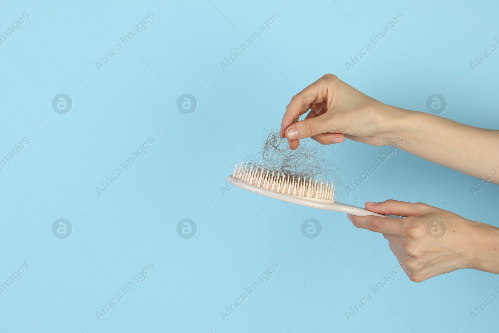 Photo of Woman taking lost hair from brush on light blue background, closeup. Space for text