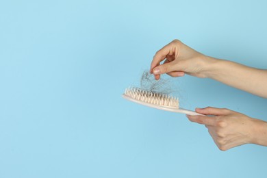 Woman taking lost hair from brush on light blue background, closeup. Space for text