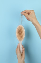 Woman taking lost hair from brush on light blue background, closeup