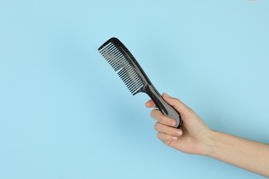 Woman holding comb with lost hair on light blue background, closeup. Space for text