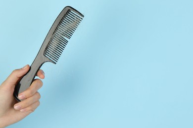 Photo of Woman holding comb with lost hair on light blue background, closeup. Space for text