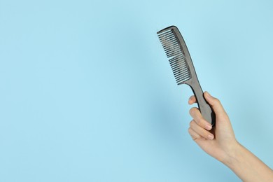 Photo of Woman holding comb with lost hair on light blue background, closeup. Space for text