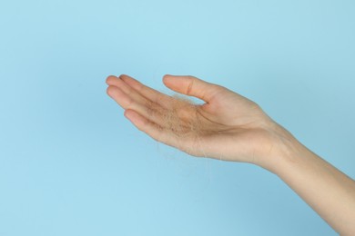 Woman holding lost hair on light blue background, closeup. Space for text