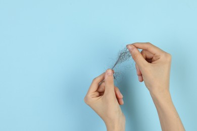 Photo of Woman holding lost hair on light blue background, closeup. Space for text