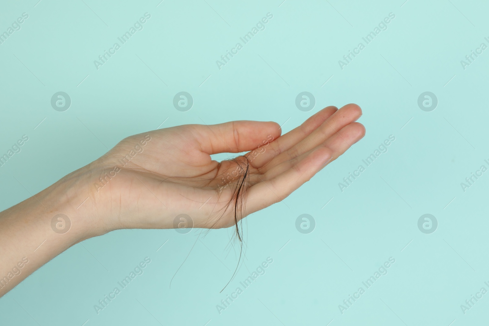 Photo of Woman holding lost hair on turquoise background, closeup. Space for text