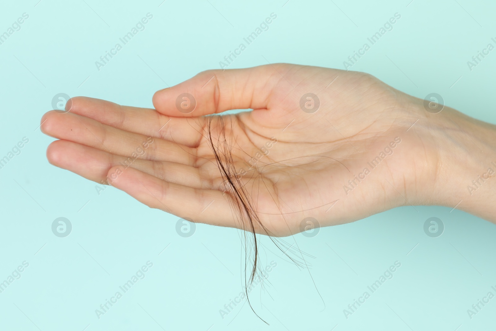 Photo of Woman holding lost hair on turquoise background, closeup