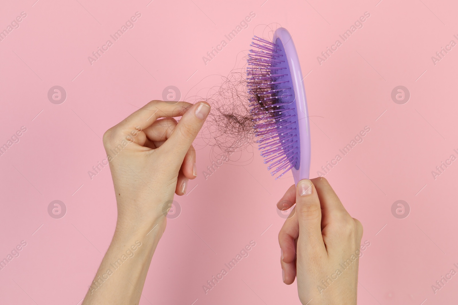 Photo of Woman taking lost hair from brush on pink background, top view