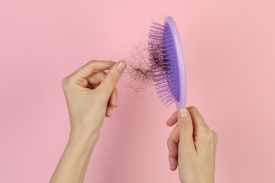 Woman taking lost hair from brush on pink background, top view