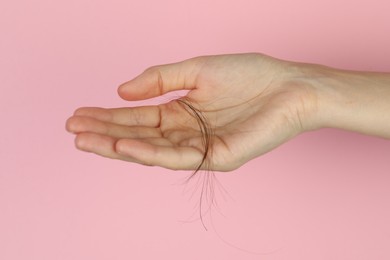 Woman holding lost hair on pink background, closeup