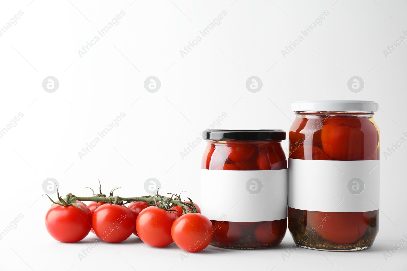 Photo of Tasty pickled tomatoes in jars and vegetables on light background. Space for text