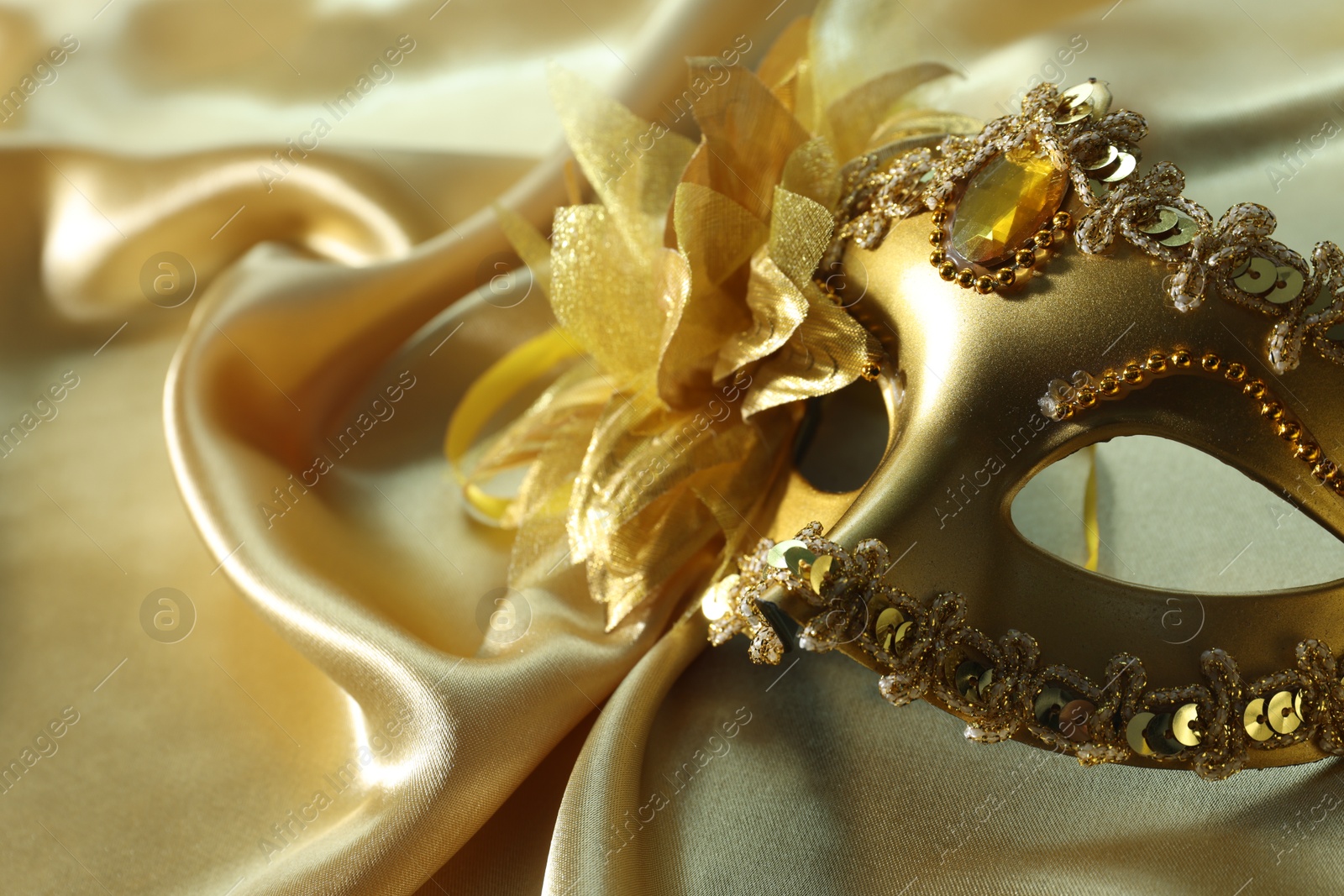 Photo of One beautiful carnival mask on golden fabric, closeup. Space for text