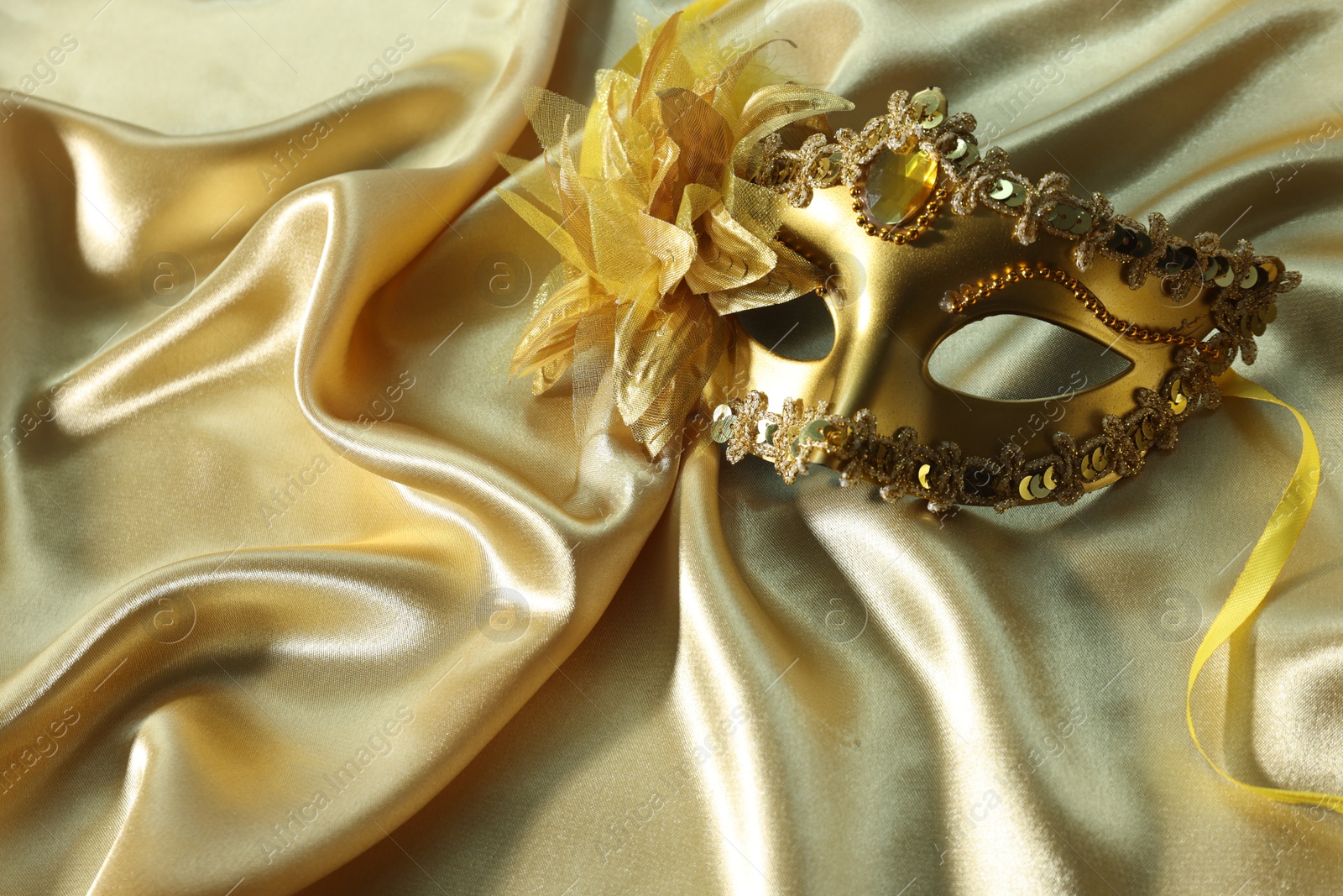 Photo of One beautiful carnival mask on golden fabric, space for text